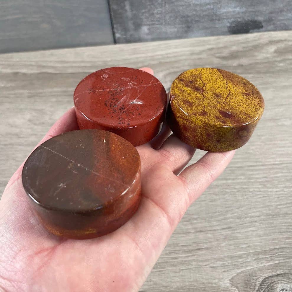Three red jasper disks held in a hand on a wooden surface