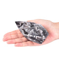 A hand holding a polished black and white geode-shaped stone, with two more similar stones blurred in the background on a white surface.