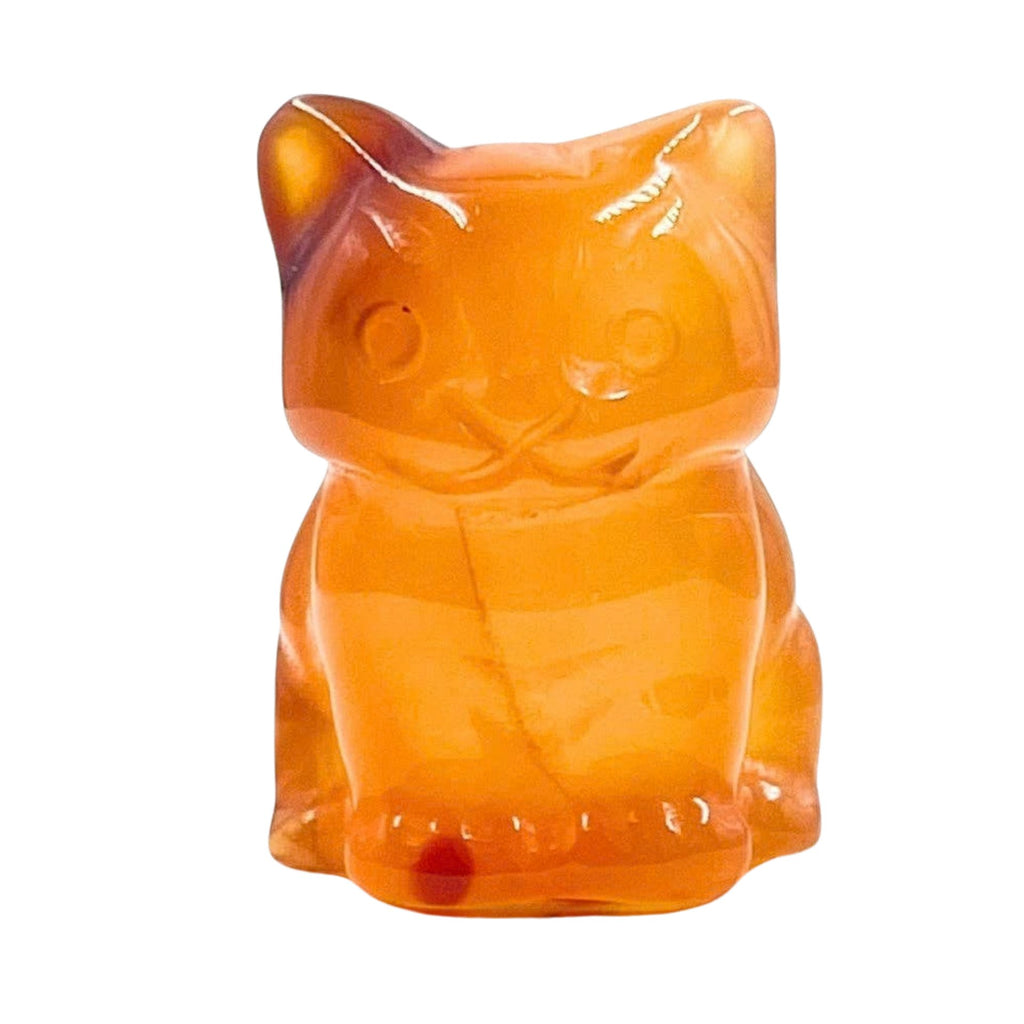 An orange translucent cat-shaped decorative object, resembling a gummy bear or candy, centered on a white marble surface with orange flowers and green leaves around it.