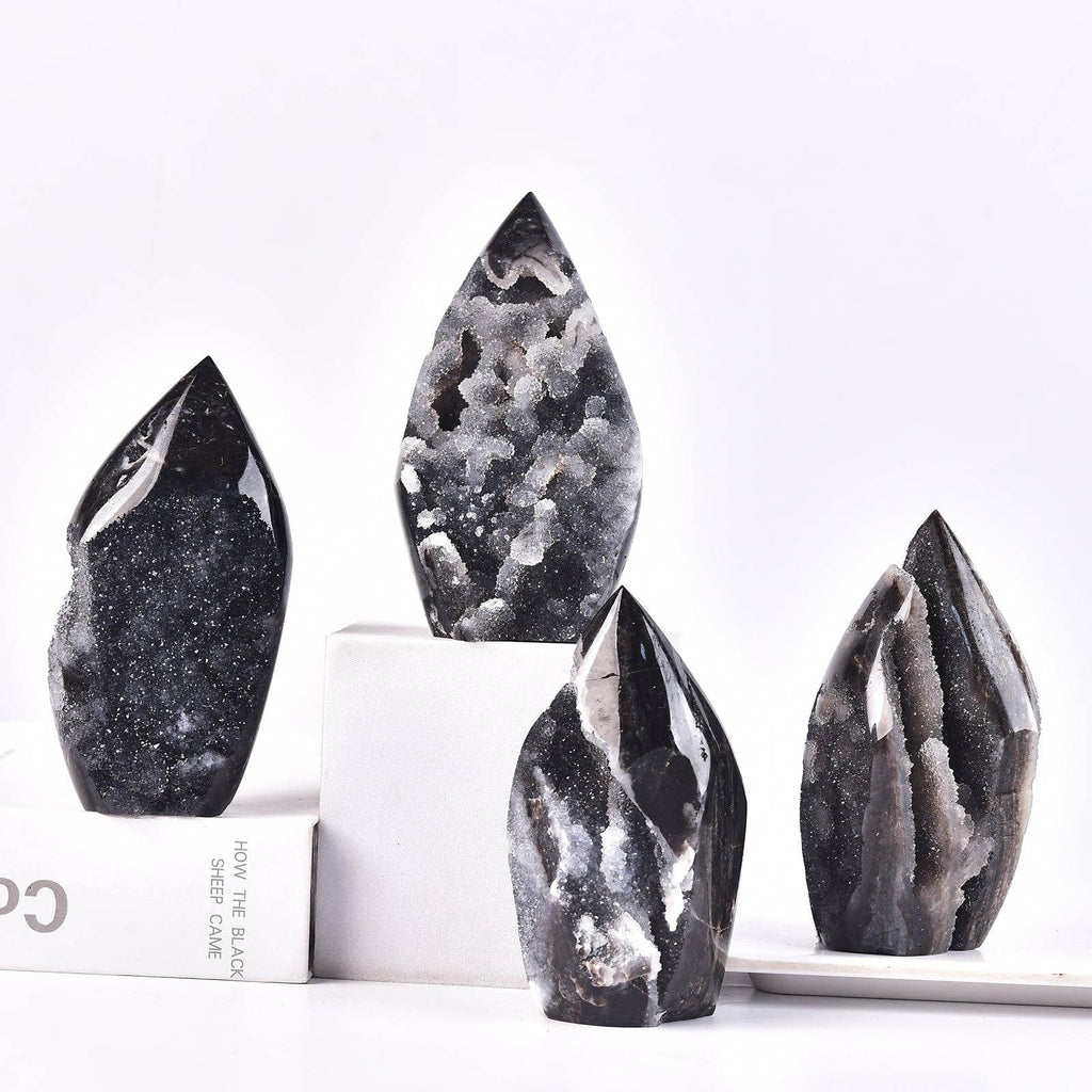Four polished black geode crystal point towers of varying heights and shapes, arranged on white display blocks and a white surface against a clean white background.