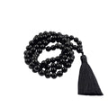 A black obsidian beaded necklace with a matching black tassel, arranged in a coil on a white surface 