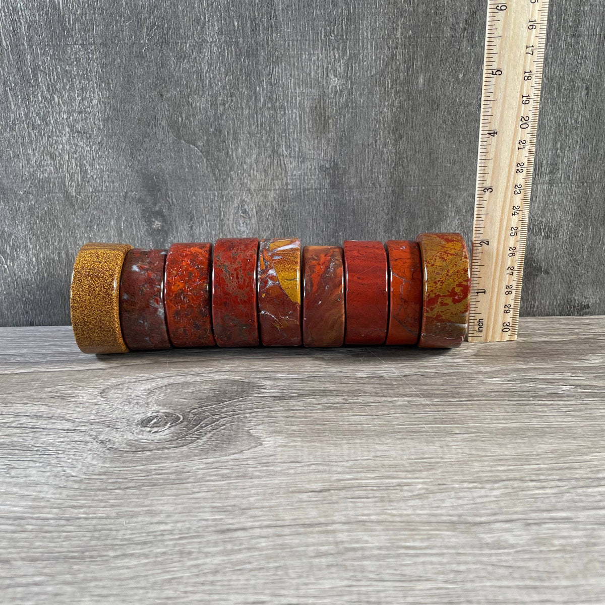 A set of eight stacked red jasper disks, shown next to a wooden ruler for scale on a gray wood-grain surface.