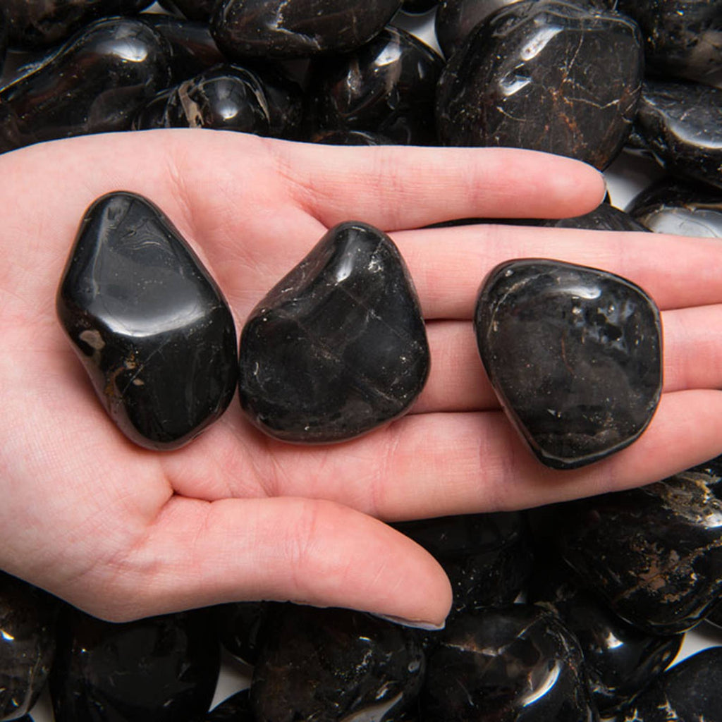 Three black onyx stones held in a hand with more stones in the background