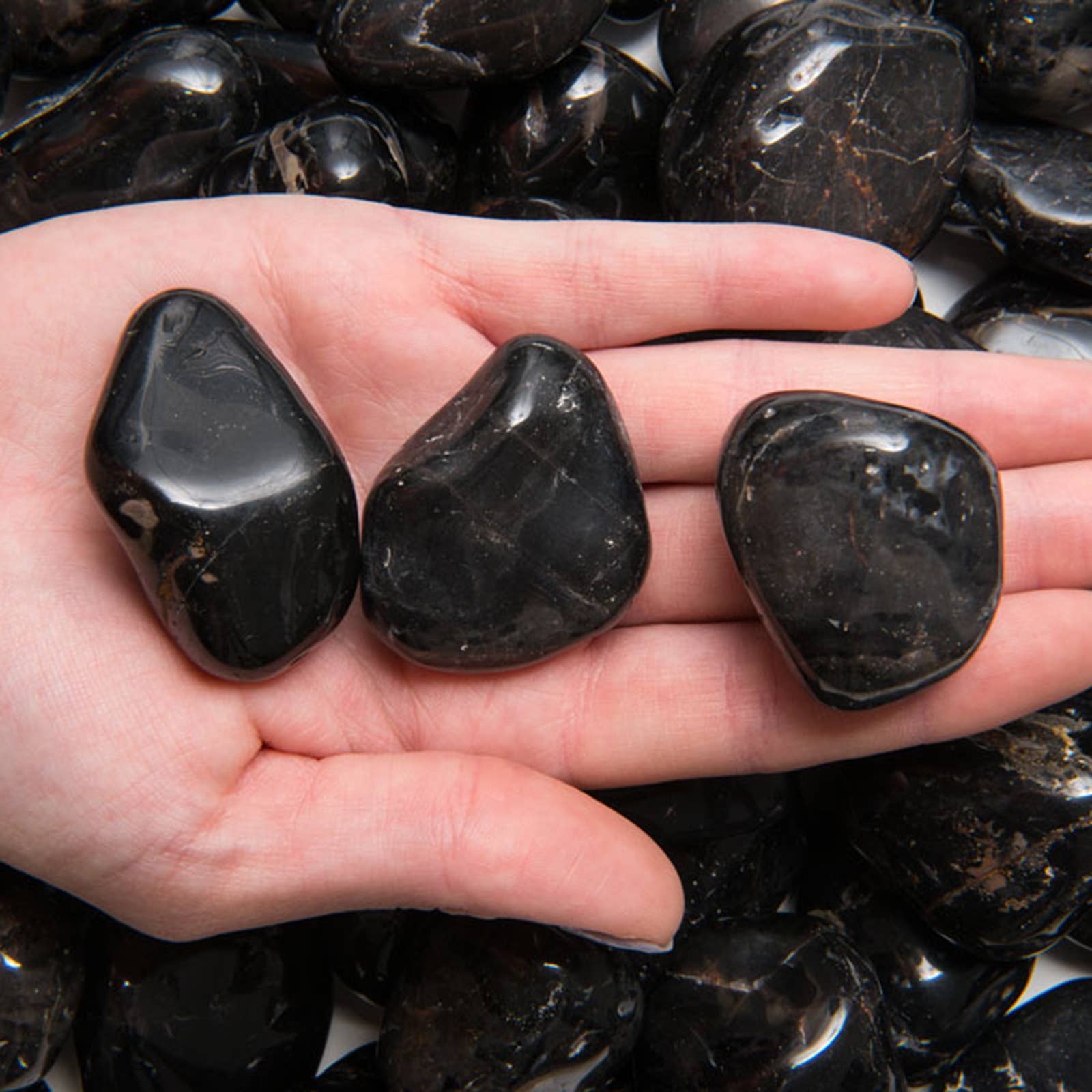 Three black onyx stones held in a hand with more stones in the background