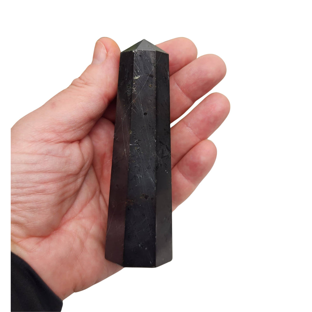 A hand holding a tall, faceted black Tourmaline crystal tower against a plain white background.