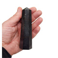 A hand holding a tall, faceted black Tourmaline crystal tower against a plain white background.