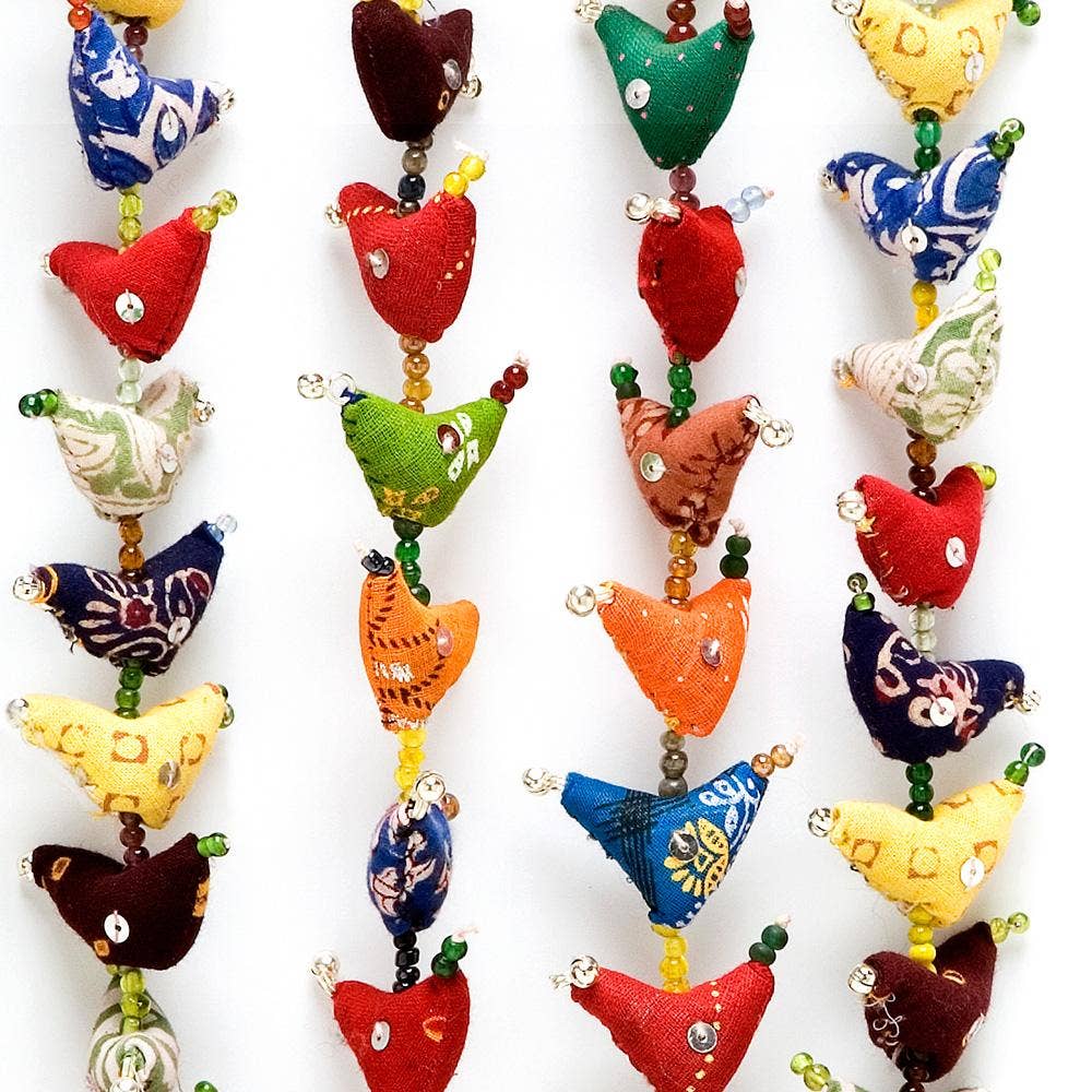 A close-up of multiple colorful fabric heart-shaped ornaments or beads strung vertically on white strings against a plain white background. The hearts are in many colors and patterns, including red, green, blue, yellow, orange, and brown, with small shiny embellishments.