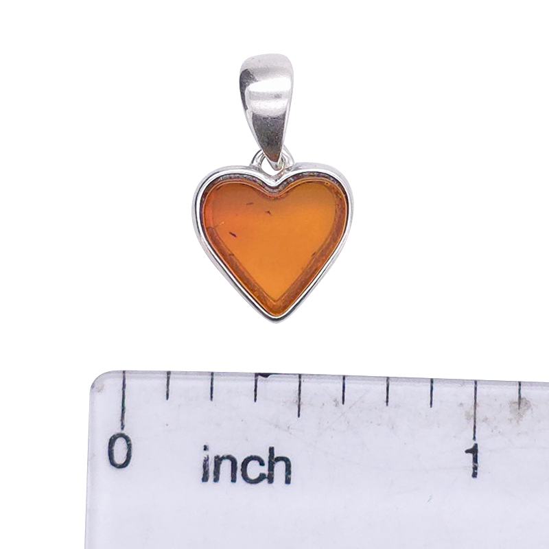 A heart-shaped amber pendant with a silver border and bail, shown above a clear ruler marked in inches to indicate scale, on a white background.