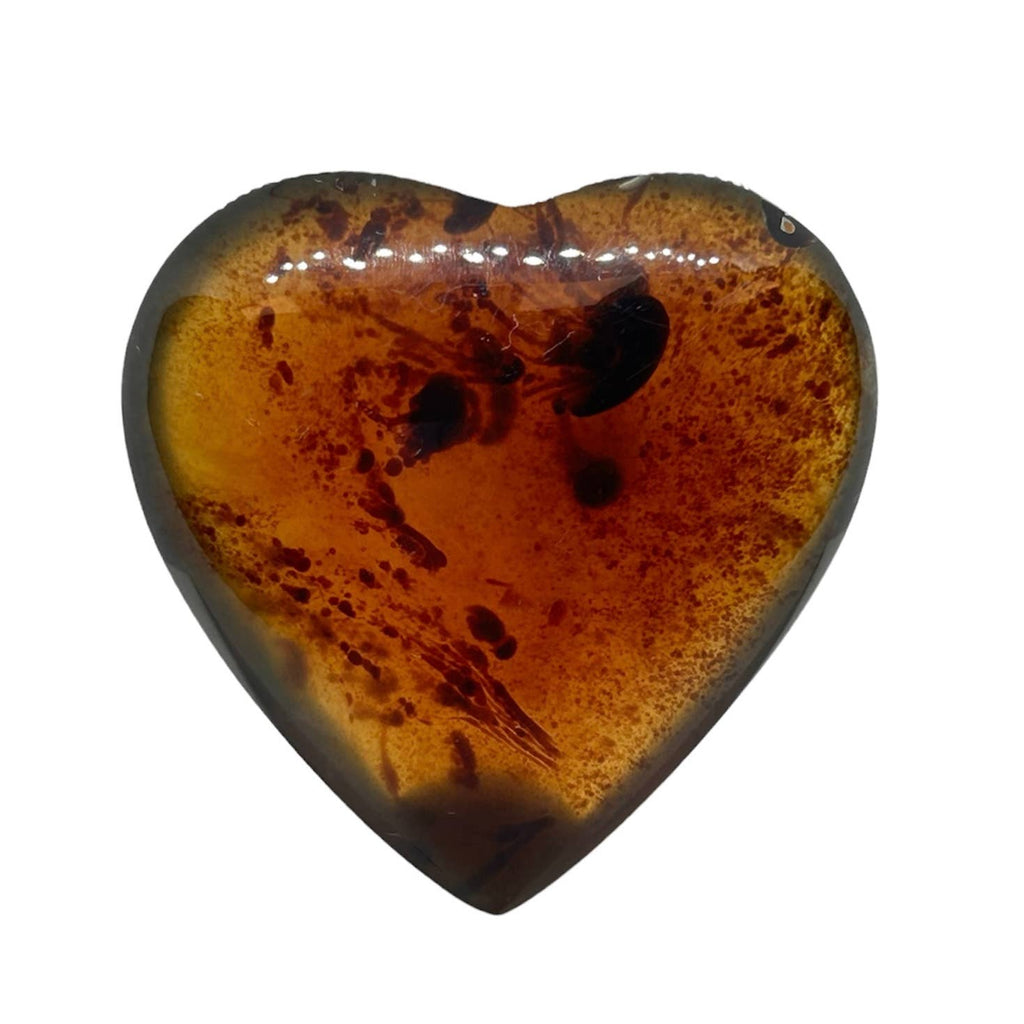 A heart-shaped polished amber with natural inclusions and dark brown spots, shown on a plain white background.