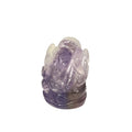 A carved amethyst figurine of a seated Buddha, showcasing a natural gradient from translucent light lavender to deep purple, set against a plain white background.