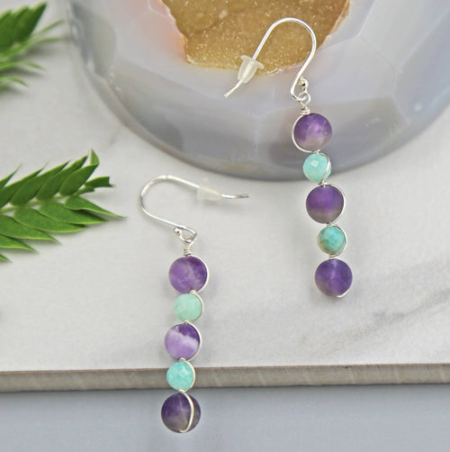 Pair of beaded earrings with amethyst and amazonite beads on a white surface with a natural background.