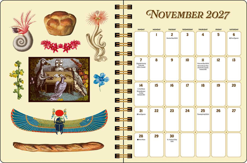 A spiral-bound November 2027 planner page with a cream background and decorative Egyptian-themed illustrations, including a scarab beetle, papyrus, bread, and floral elements alongside a blank monthly calendar grid.