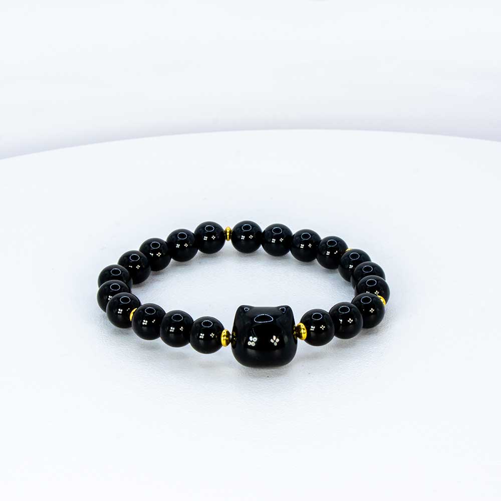 A black beaded bracelet with a central black cylindrical charm featuring white star-like details, separated by small gold spacer beads, displayed on a clean white background.