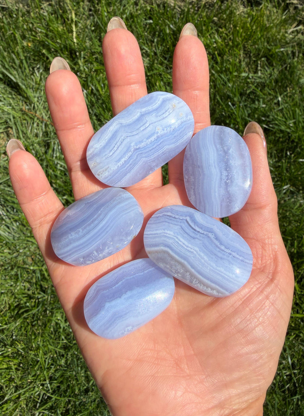 Hand holding five blue stones against a grassy background