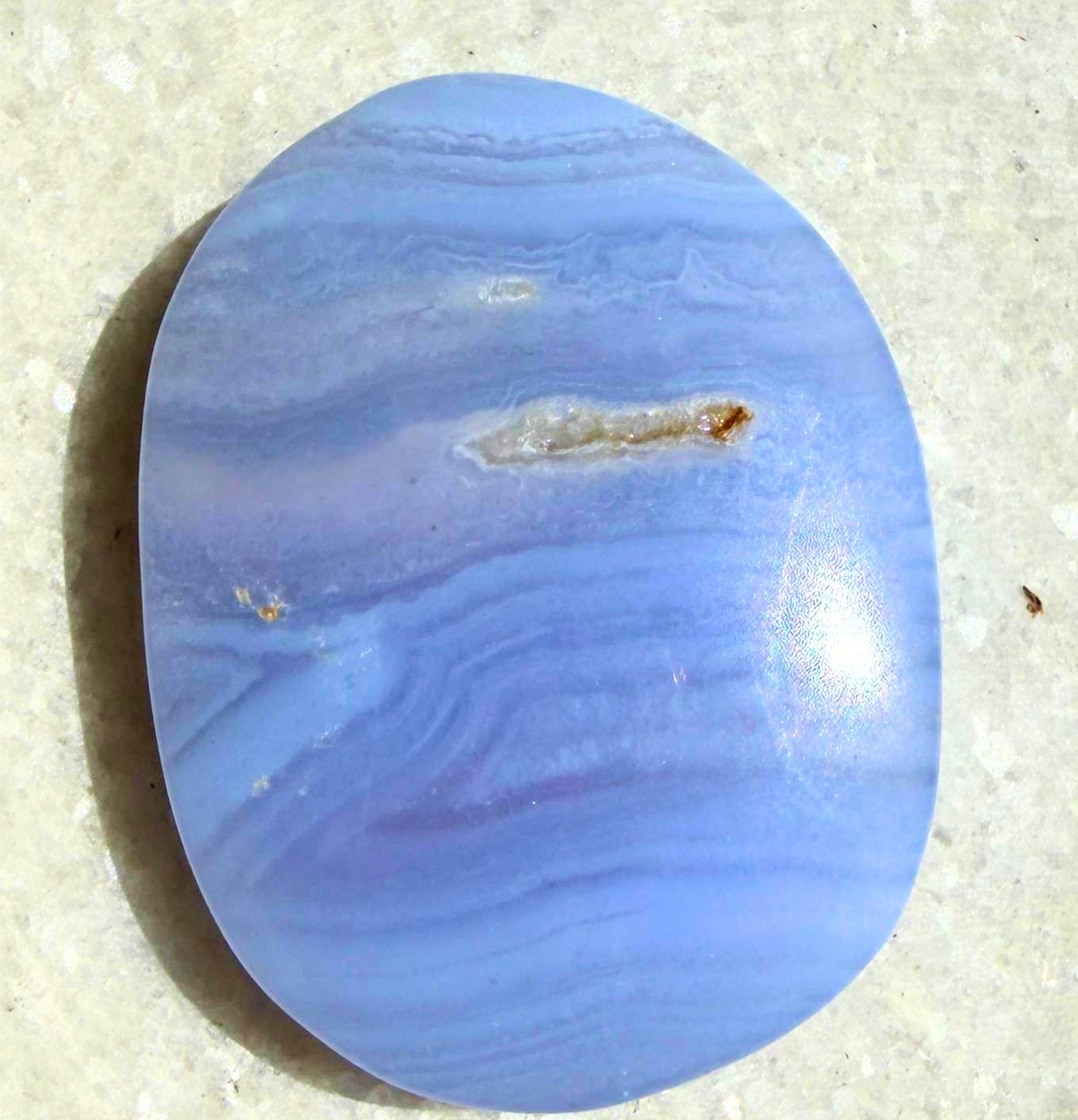 Blue lace Agate palm stone with swirling patterns on a gray concrete surface