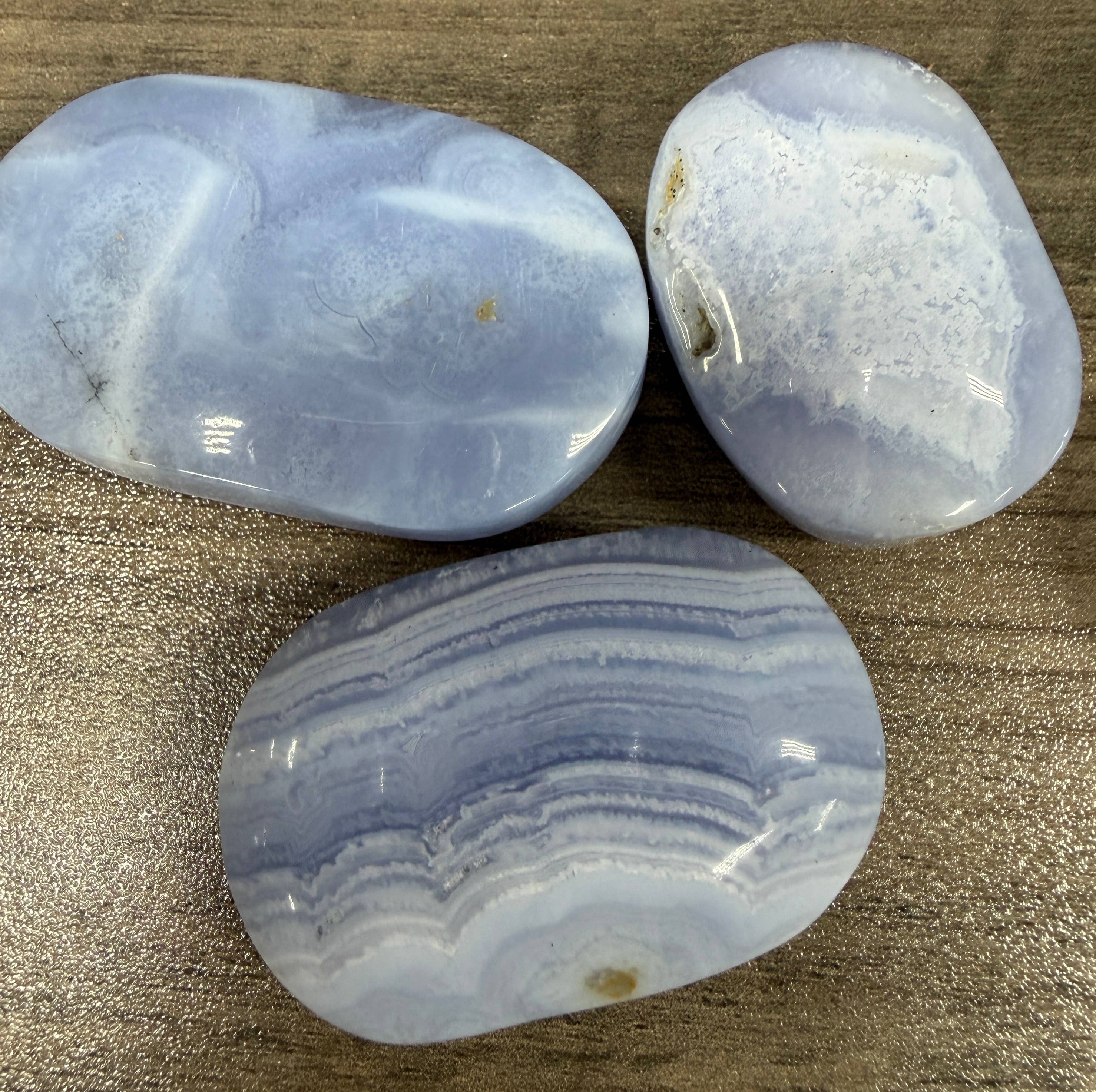 Three blue and white striped Blue Lace Agate Palm stones on a brown surface