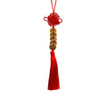 A red Chinese knot hanging ornament with a red tassel and a central decorative cylindrical section featuring gold and red Chinese characters, isolated on a white background.