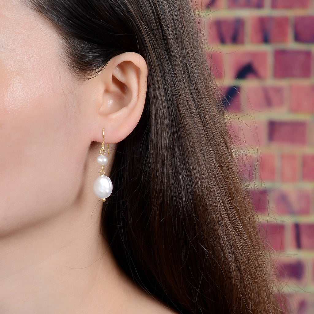 Close-up of a person wearing pearl earrings with a brick wall background