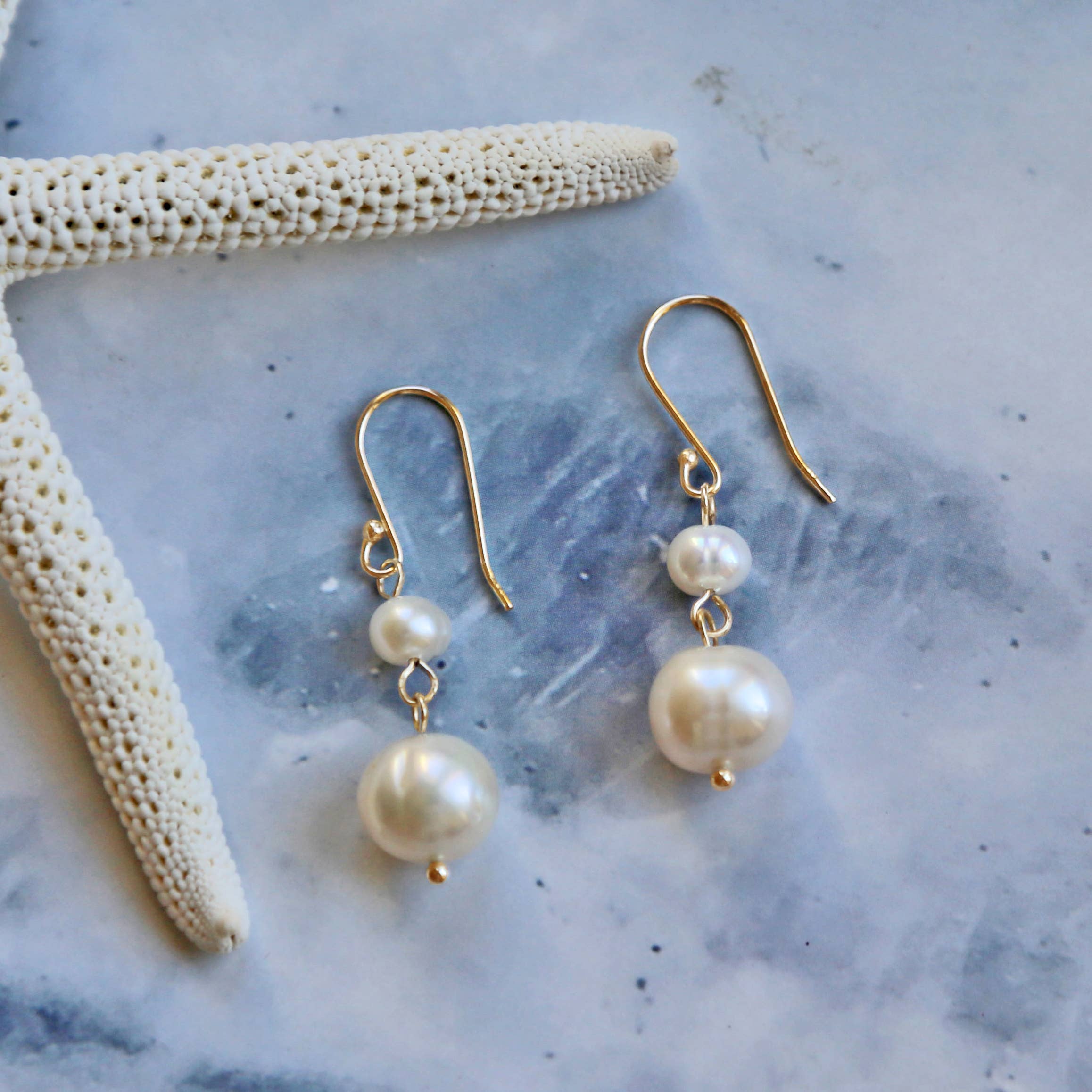 Pearl earrings with gold hooks on a textured surface with starfish
