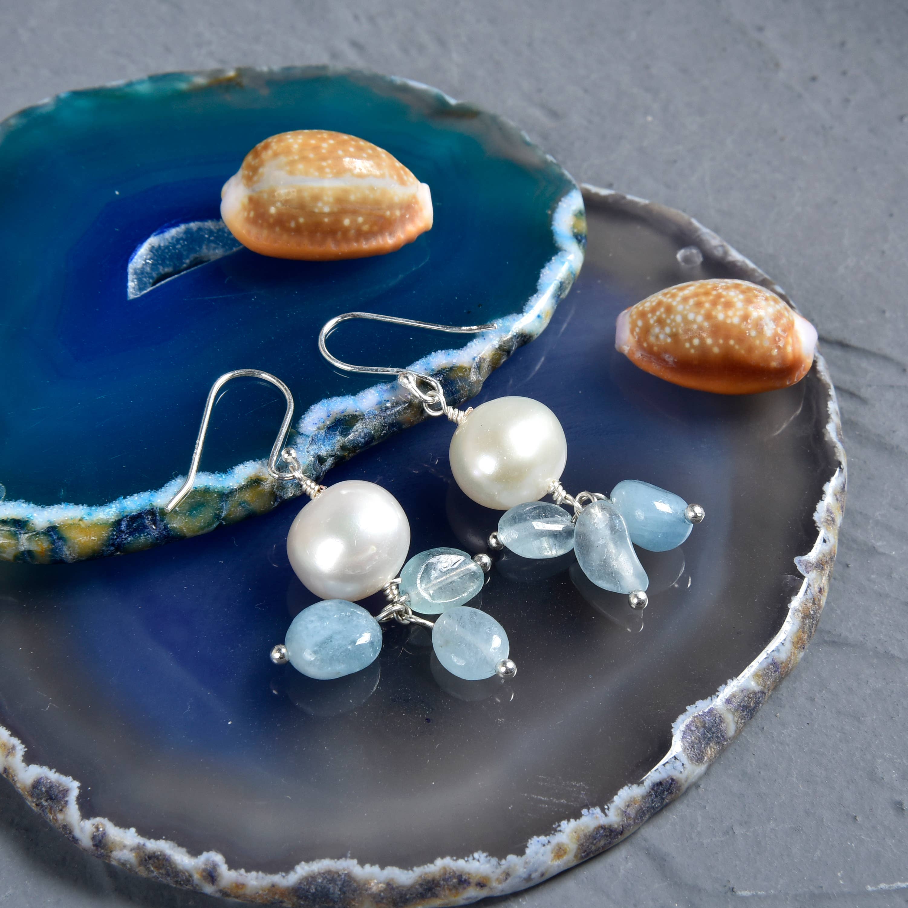 Pearl and gemstone earrings on a decorative stone surface with shells.