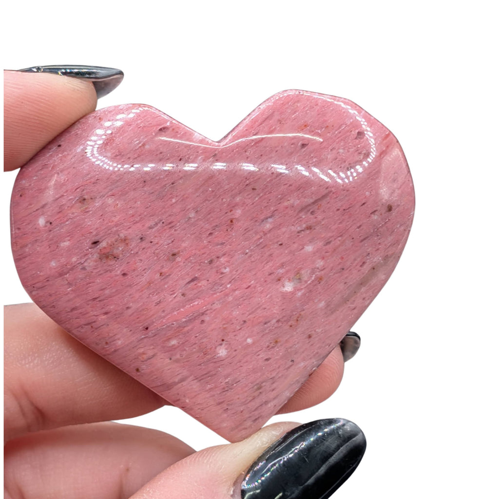 A hand holds a polished, pink, heart-shaped petrified wood stone