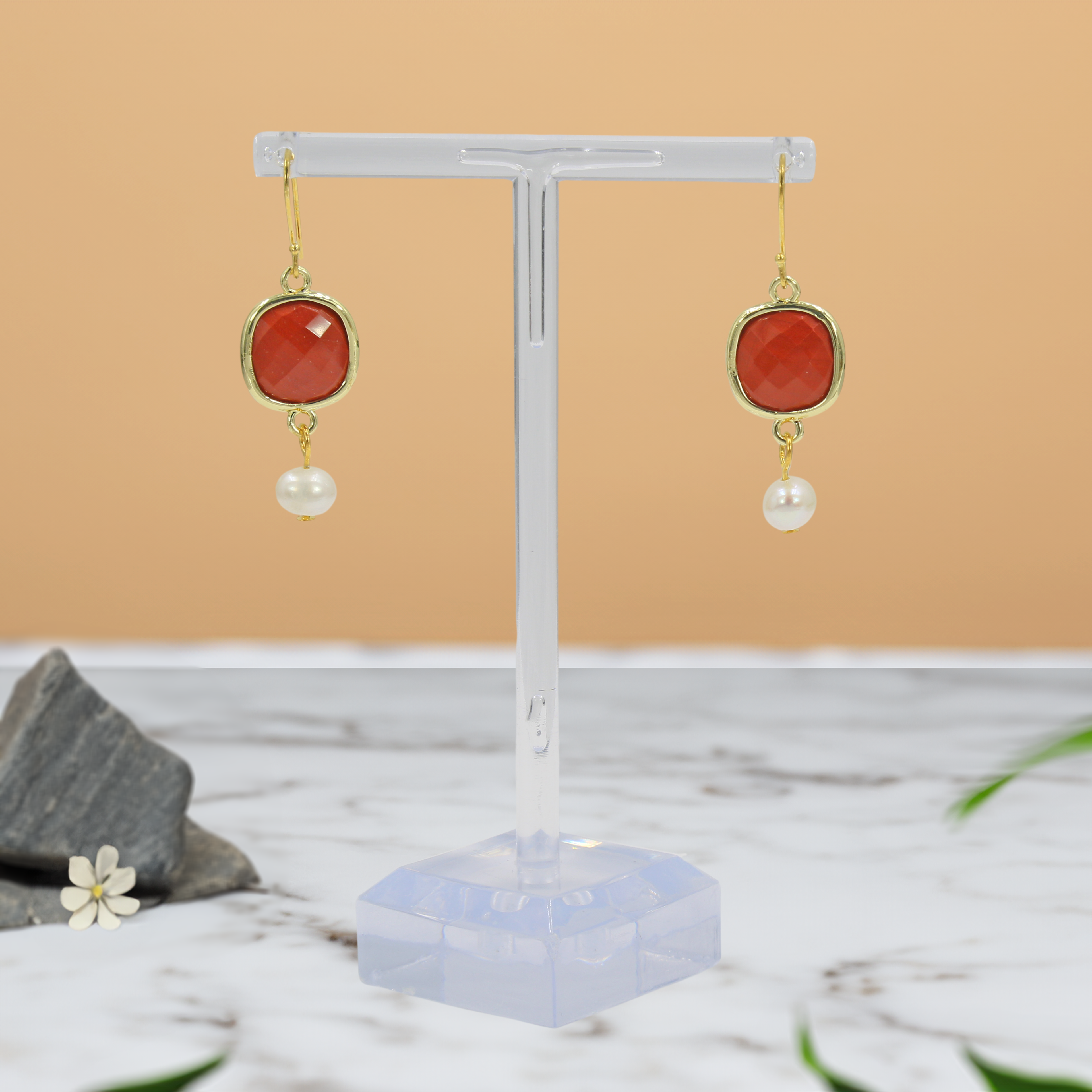 Pair of earrings with red stones and pearls on a clear stand against a beige background