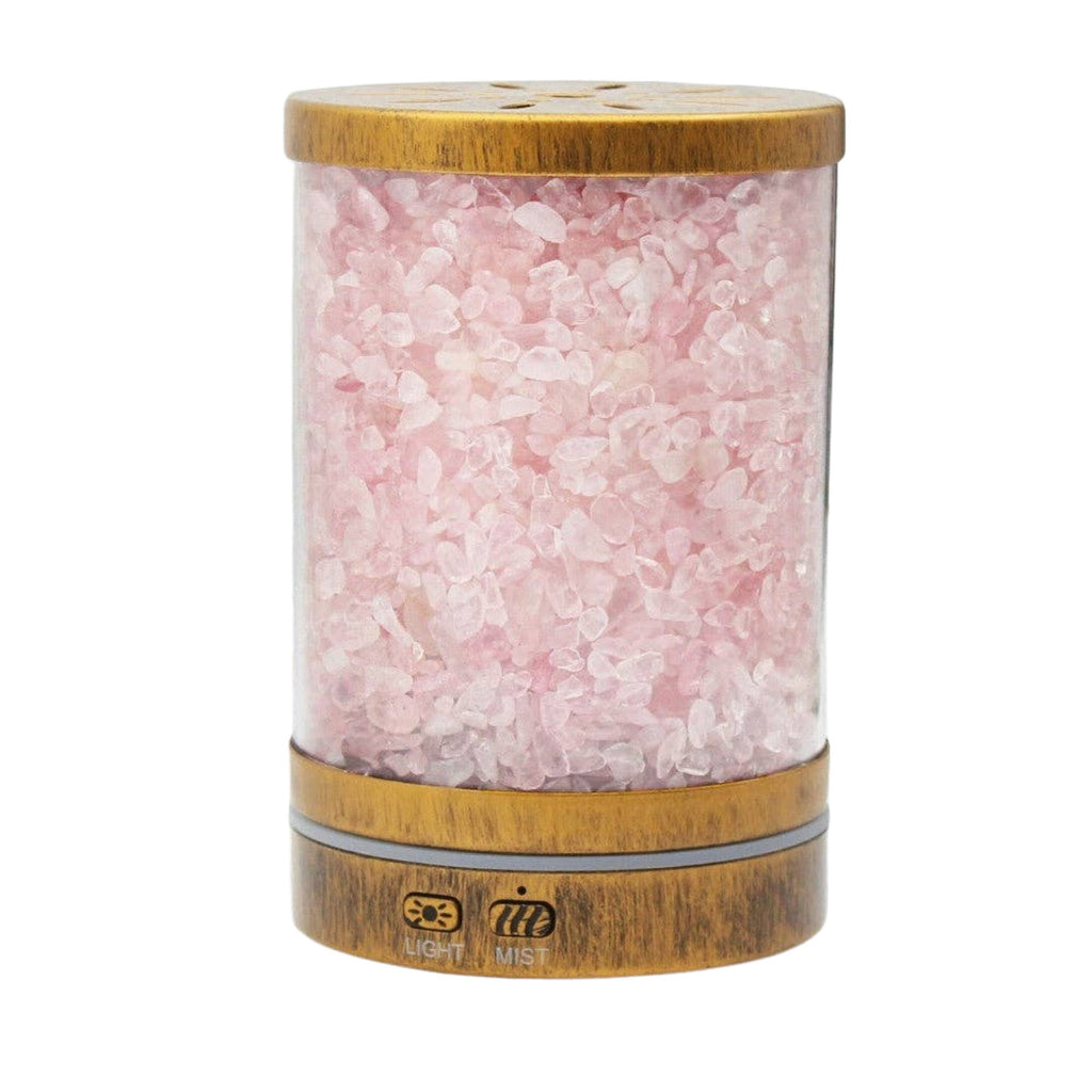 A cylindrical diffuser filled with pink rose quartz crystals, featuring a light brown bamboo top and bottom with a small LED light indicator on the front, set against a plain white background.