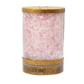 A cylindrical diffuser filled with pink rose quartz crystals, featuring a light brown bamboo top and bottom with a small LED light indicator on the front, set against a plain white background.