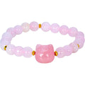 A pink beaded bracelet featuring a central faceted pink stone bead shaped like a cat head, accented by small gold spacer beads on a white background.