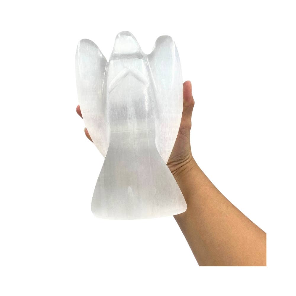 A hand holding a selenite angel-shaped lamp against a plain white background.