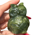 A hand holding a small carved green Serpentine owl figurine against a plain white background.