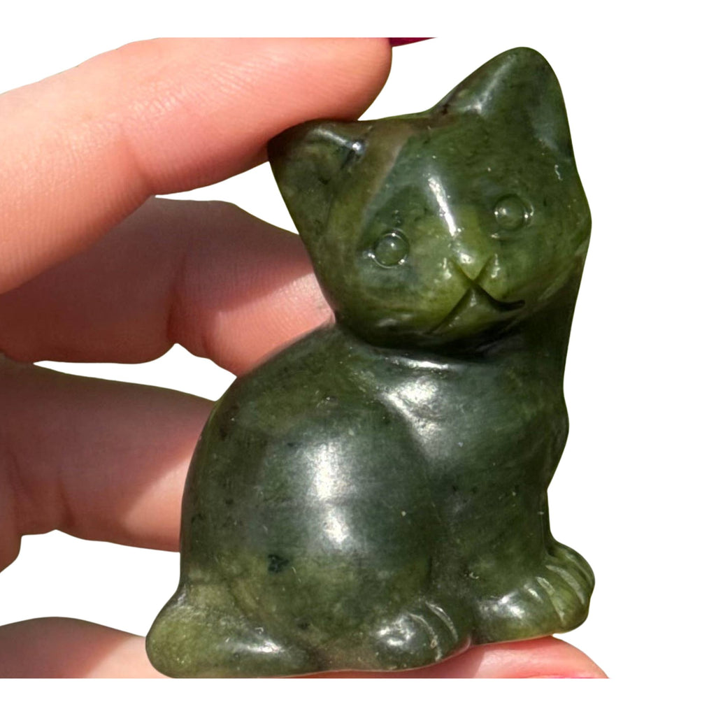 Sepentine cat figurine held between fingers with a blurred green leafy background