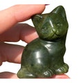 Sepentine cat figurine held between fingers with a blurred green leafy background