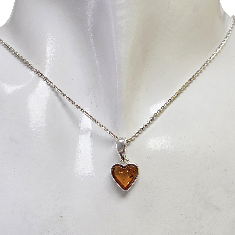 A silver chain necklace with a heart-shaped amber pendant, displayed on a white mannequin bust.
