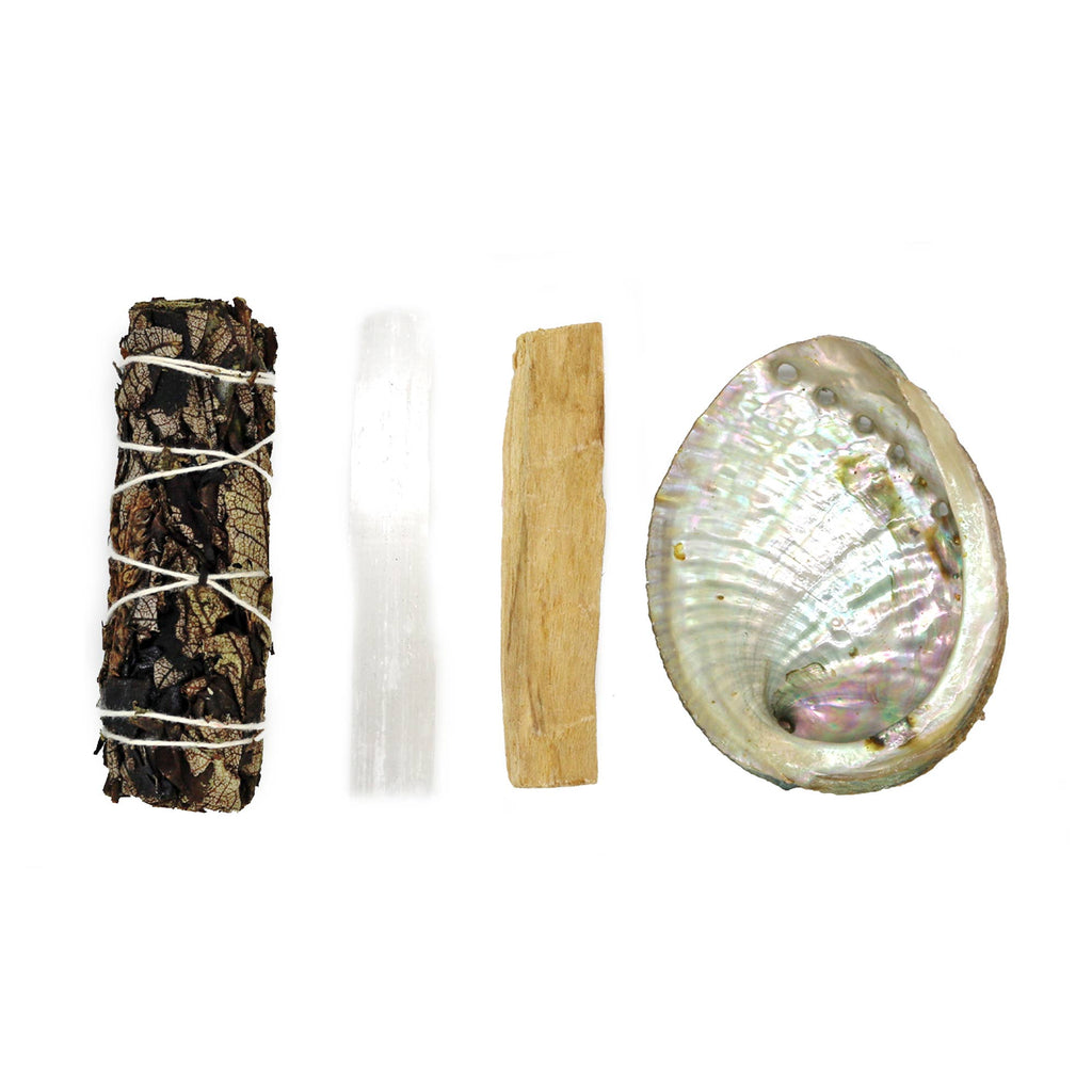 Set of spiritual tools including a sage bundle, crystal, palo santo stick, and abalone shell on a white background