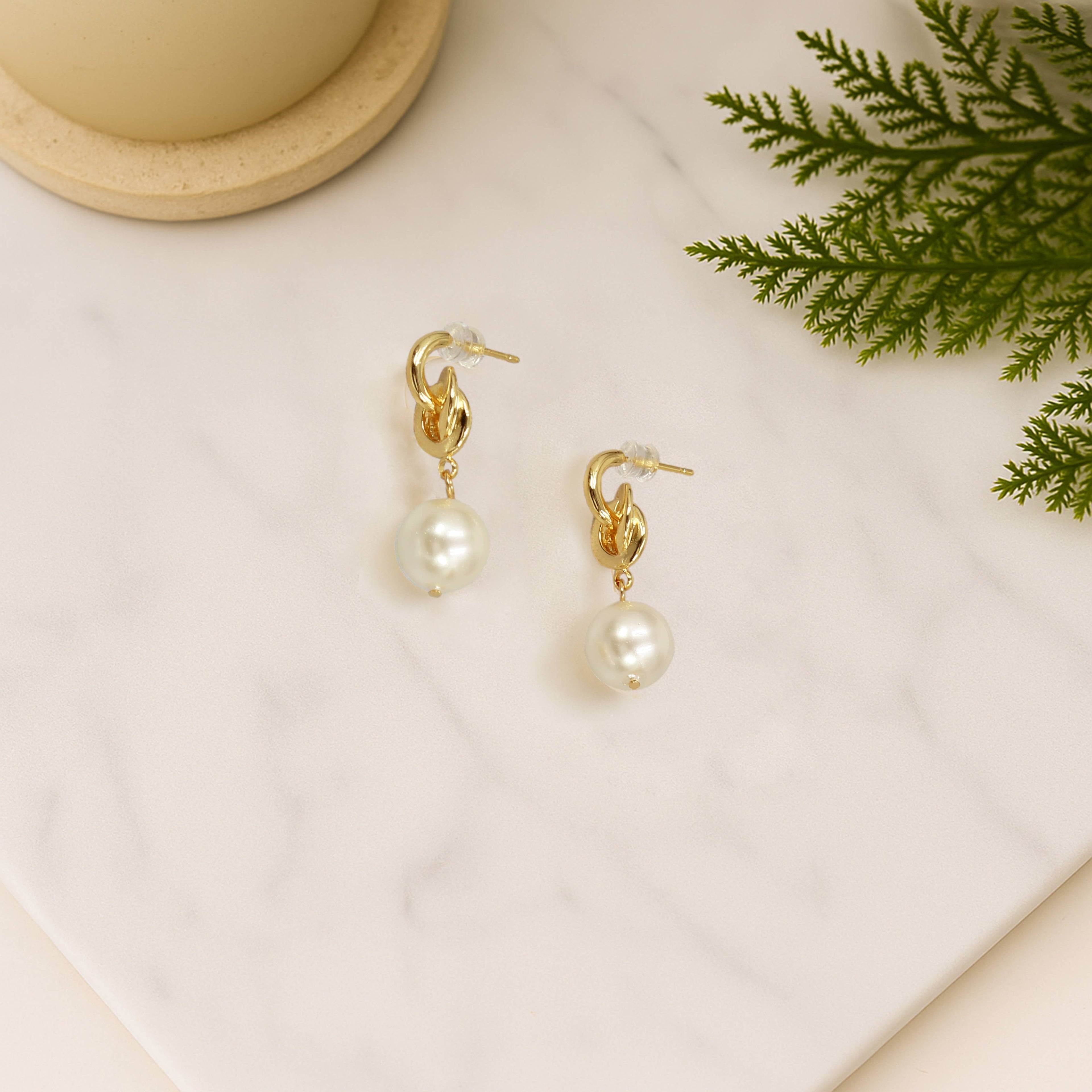 Gold earrings with pearls on a light surface with greenery