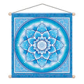 A square hanging wall tapestry featuring a detailed blue and white mandala design with a central geometric symbol. The tapestry is suspended by a black cord from two wooden wall mounts with light beige balls, shown against a plain white background.