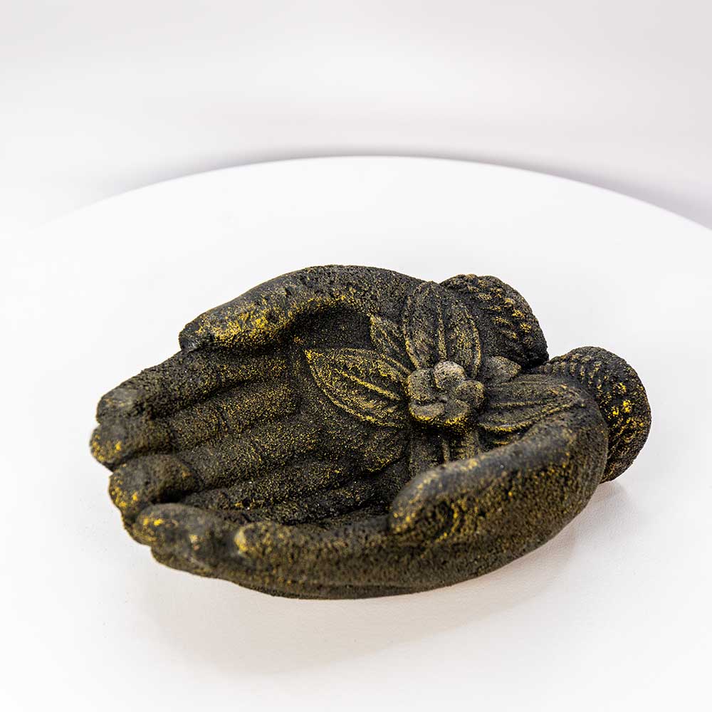 A decorative resin sculpture of two hands cupping a small flower, finished with a textured metallic gold and dark bronze finish, displayed on a white surface.