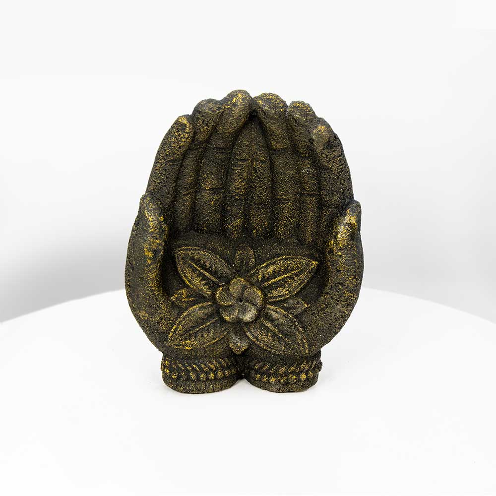 A small decorative sculpture of praying hands holding a flower, finished in a textured dark metallic finish with gold speckling, set against a plain white background.