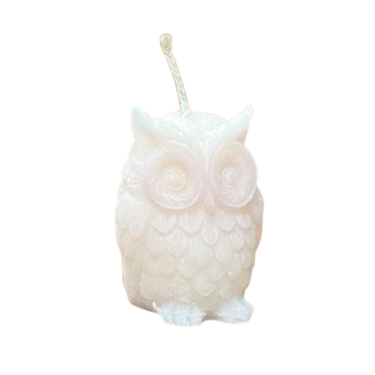 A small white owl-shaped candle with a wick, standing on a wooden tabletop against a dark blurred background.