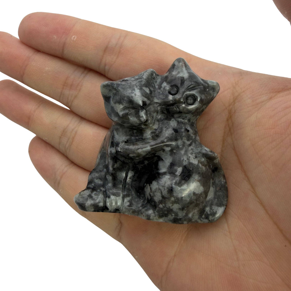 A small carved stone figurine of two crouching cats, held in a person's hand against a plain light background.