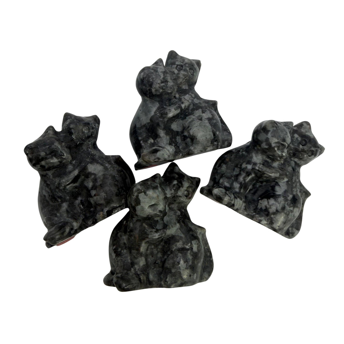 Four carved stone figurines shaped like cats, made from dark marbled yooperlite stone with black, gray, and white patterns, arranged on a plain white surface.