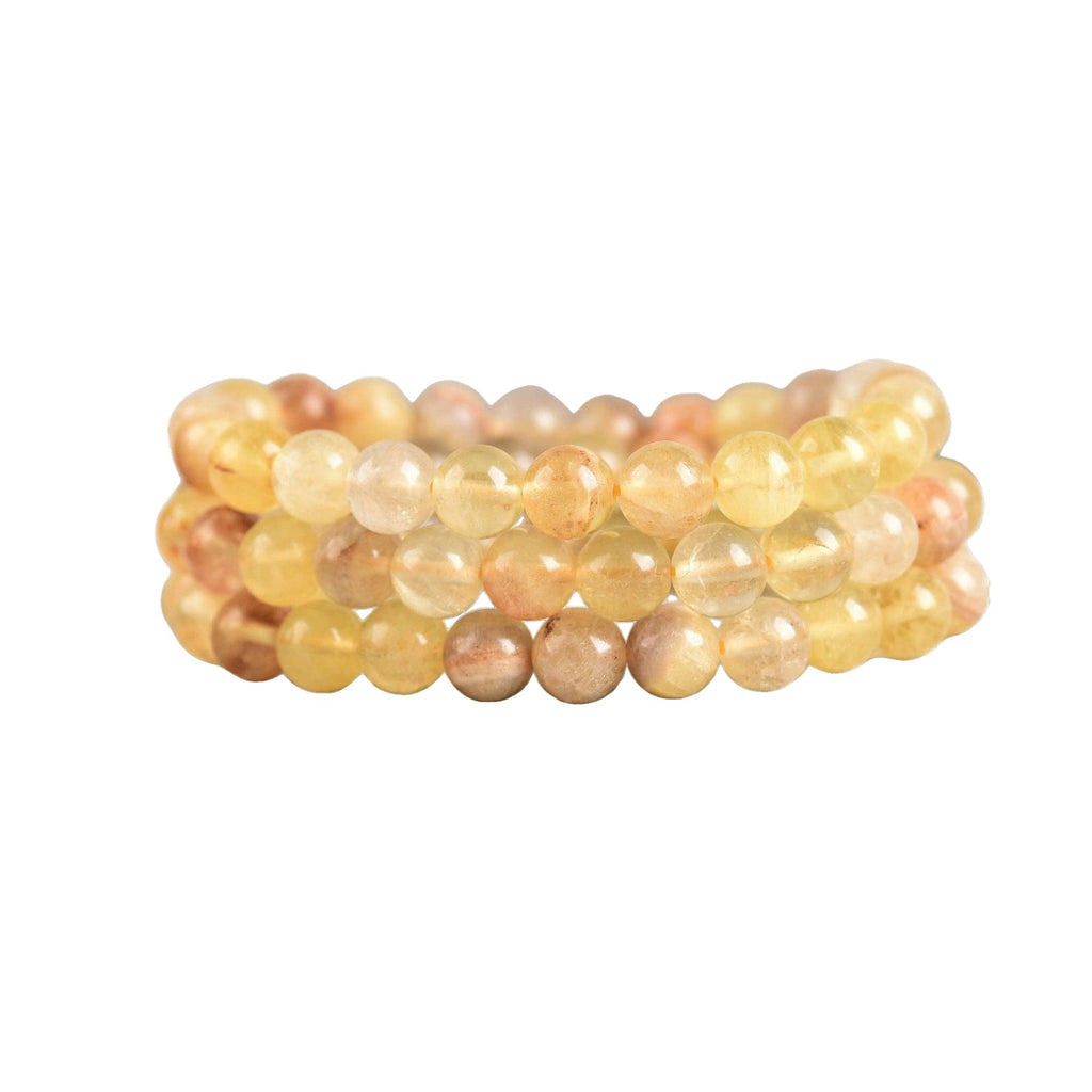 Three stacked beaded stretch bracelets made of translucent yellow fluorite round stones in soft yellow, peach, and warm beige tones,  on a white background.