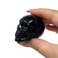 Hand holding a black obsidian skull-shaped object against a white background
