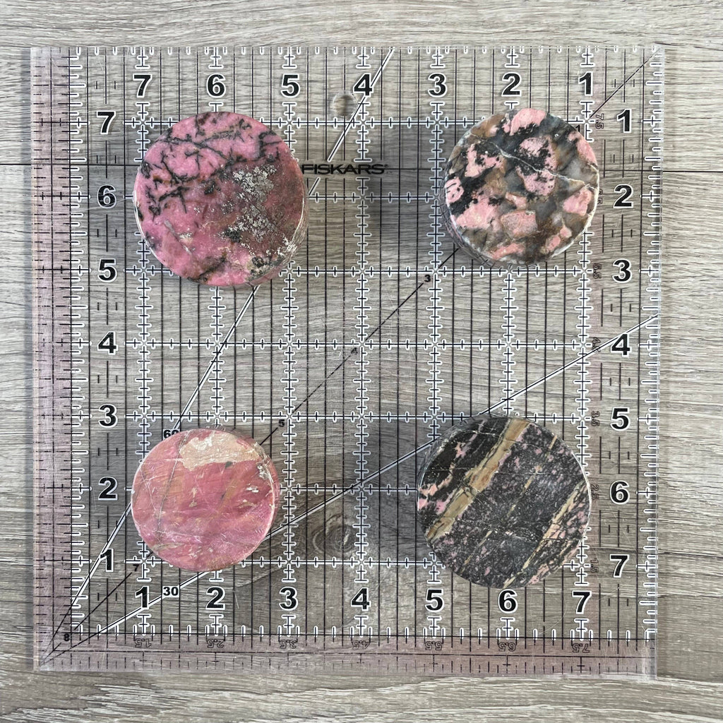 Four rhodonite stones on a ruler for size reference on a wooden surface