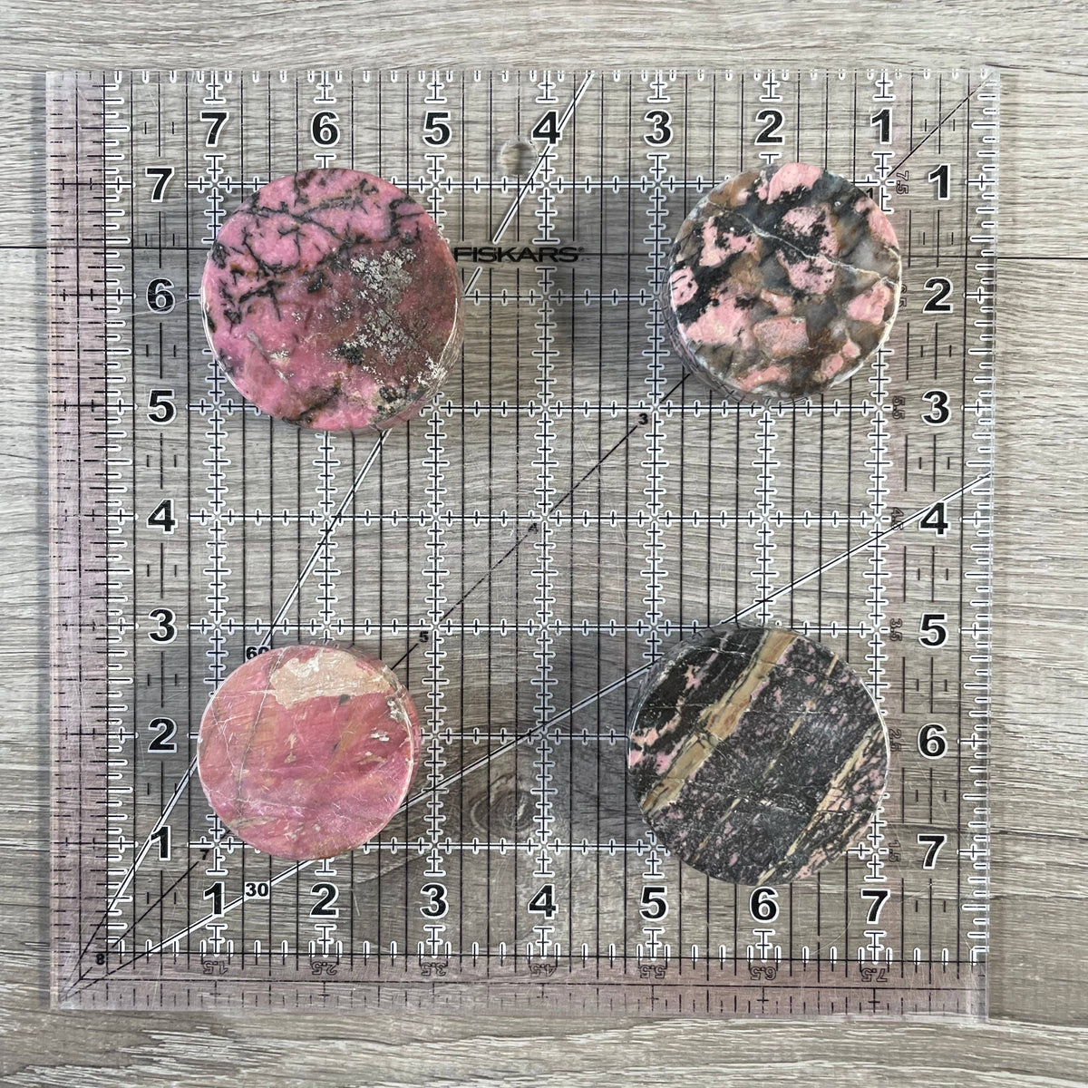 Four rhodonite stones on a ruler for size reference on a wooden surface